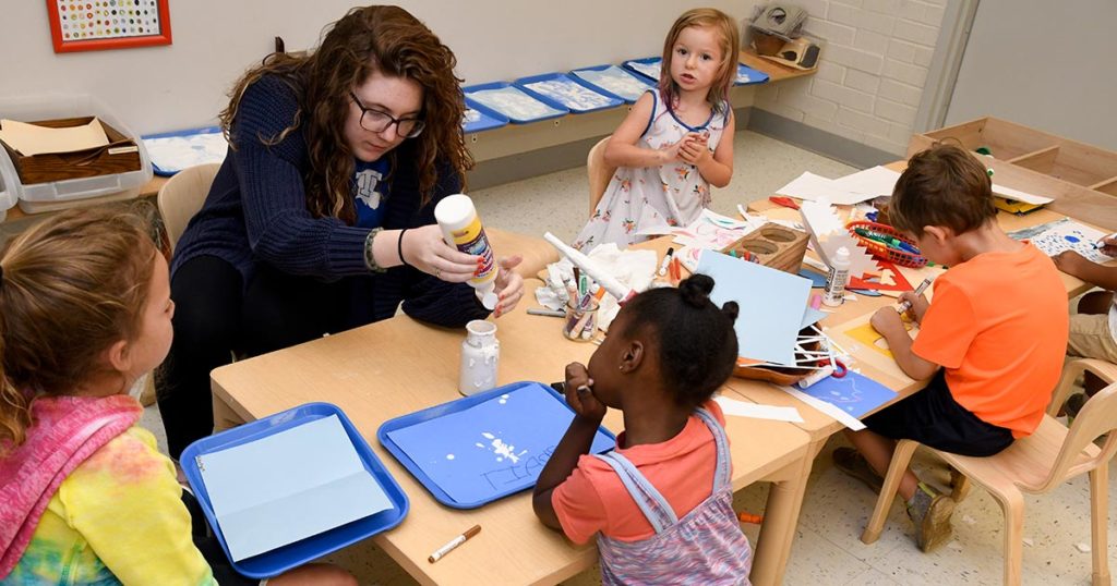 female Tech student helping kids with arts and crafts.