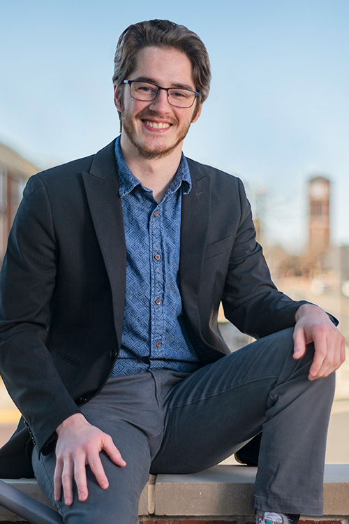 Jesse Webb is sitting on the steps of Tech Pointe II with Centennial Tower in the background.