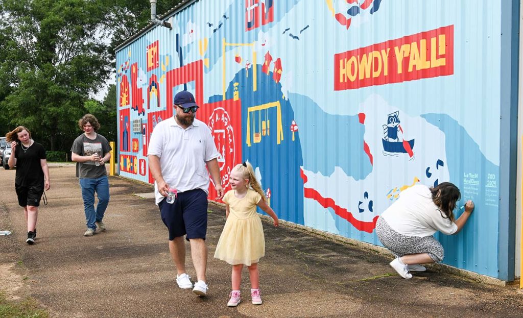 Camper M’Lynn Causey and her father pictured in front of the colorful mural at the Fire Station behind Camp Alabama.