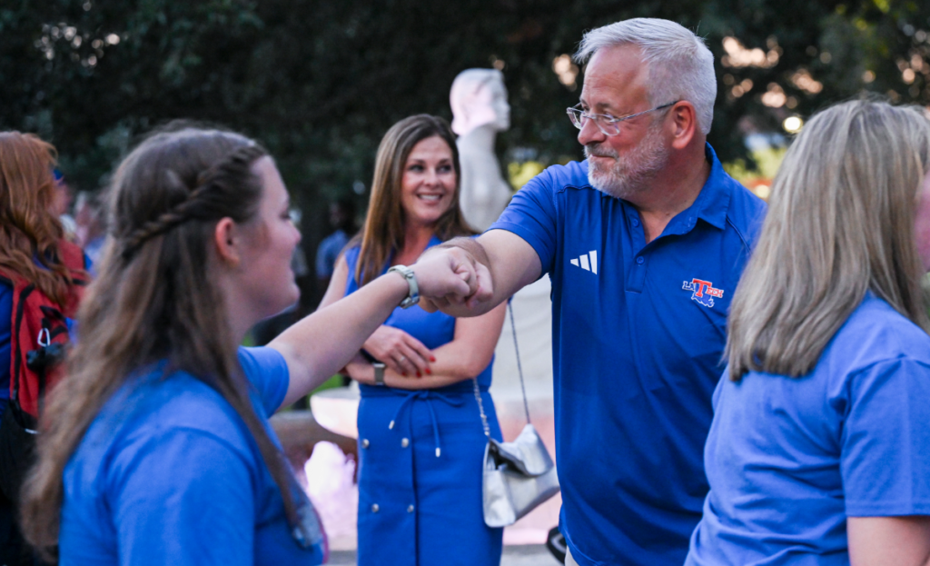 President Henderson fist bumps a freshman student in front of the Lady of the Mist in the Quad