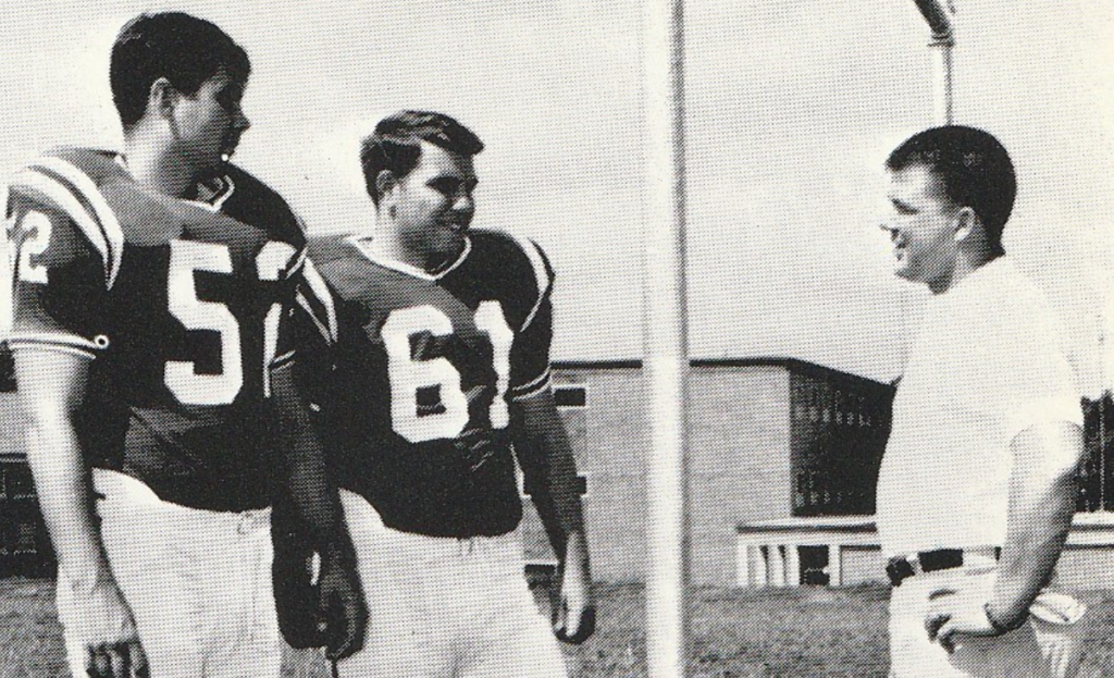 Football players, Peace and McKinnon, standing on the field talking with Coach Johnson.
