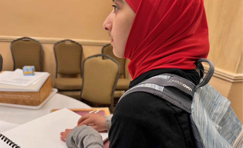 A student reading a braille story aloud to the audience at a convention. 