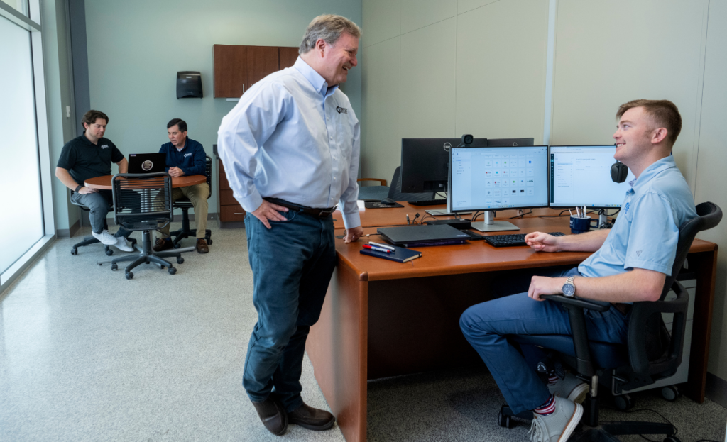 James Evans and Daylon Bozeman at a desk with two people looking at laptop in the background